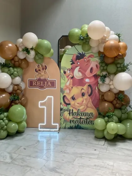A Lion King first birthday party featuring character cutouts of Simba, Timon, and Pumbaa, along with a "1" marquee number.