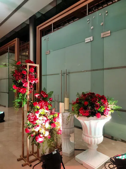 A corner floral arrangement combining a tall stand with red flowers and a classic white urn. Mirrored pedestals and candles complete this elegant vignette in the event hall.