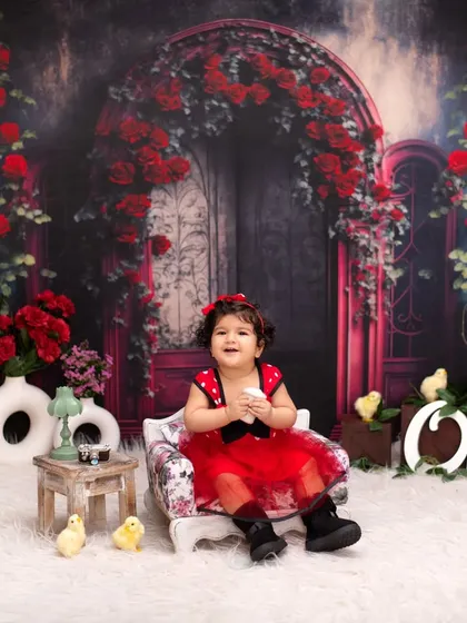 A fairytale first birthday portrait. Set against a romantic backdrop of red roses, this little one looks like she's stepped right out of a storybook in her beautiful red and black dress.