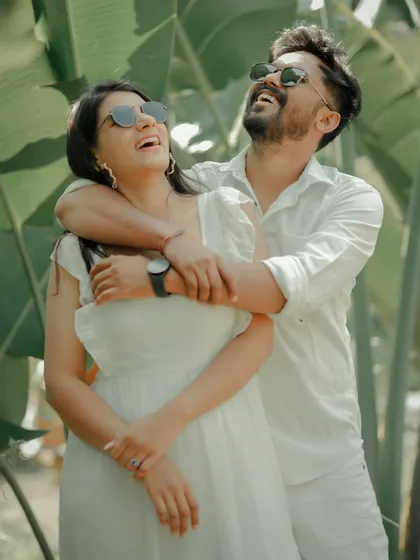 A moment of shared laughter and joy. This candid shot captures the couple in coordinated white outfits, their happiness radiating against a backdrop of tropical plants.