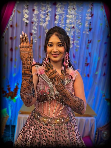 A happy bride showing off her gorgeous full arm mehndi. The design features a detailed cityscape on the back of her hands, a unique touch for a modern bride, paired with traditional patterns along the arms.