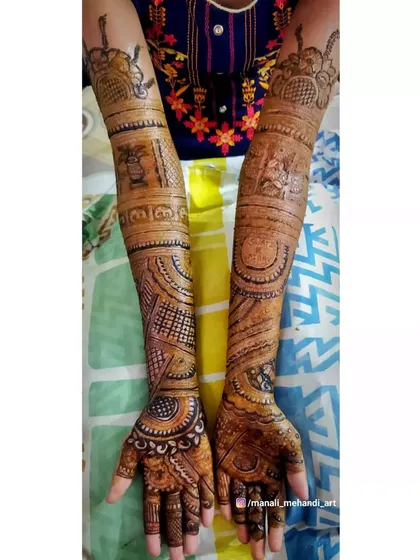 A complete view of a bridal mehandi with full arm coverage. The design includes traditional elements like a doli and kalash, along with the groom's name on the palm.