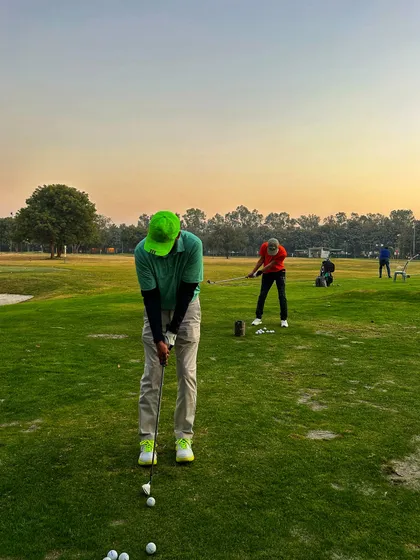 A golfer in a bright green cap lines up his shot on the grass, with a friend practicing nearby.