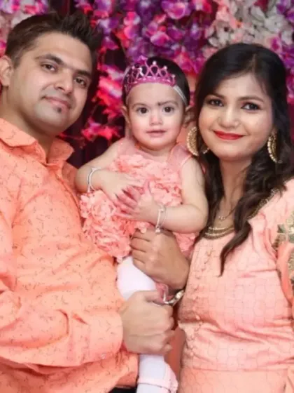 A family of three in matching peach-colored outfits pose for a portrait at a birthday event.