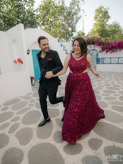 A fun, energetic moment at a location with Santorini-inspired architecture. The vibrant colors and playful action make for a joyful and memorable pre-wedding photo.