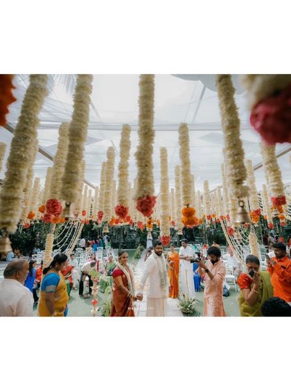 A wide shot of the wedding ceremony in progress, showing guests seated as the couple participates in rituals under the canopy of flowers.