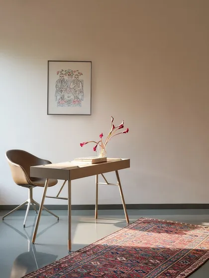 A minimalist study corner featuring a sleek desk, a modern swivel chair, and a vintage Kurdish rug, embodying the blend of old and new.