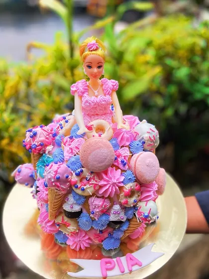 A dream come true for any Barbie fan. This cake features a Barbie doll whose dress is made entirely of colorful frosting, macarons, and edible decorations.