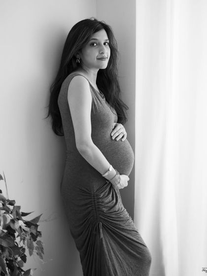 A simple, elegant portrait by the window. This black and white image has a timeless quality, focusing on her serene expression and beautiful baby bump.