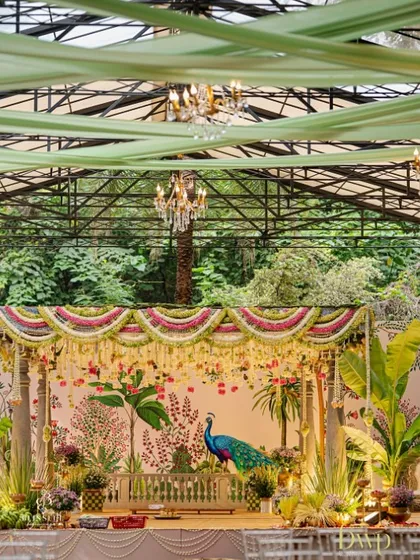 A full view of the traditional South Indian mandap, showcasing the intricate floral torans, classic temple pillars, and the beautiful hand-painted backdrop. We draped the ceiling in soft green fabric to complement the natural surroundings.