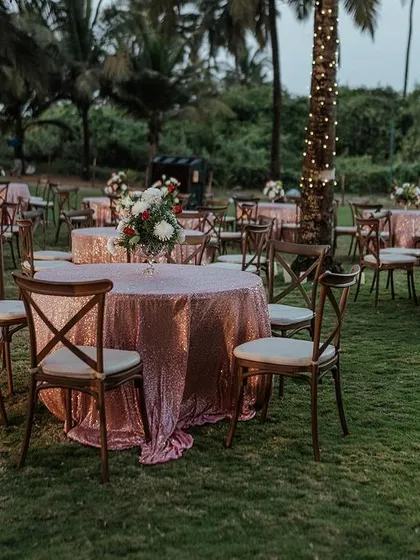 An elegant evening reception setup on a lush lawn by the beach. The sequined tablecloths and simple floral centerpieces add a touch of glamour to the outdoor setting.