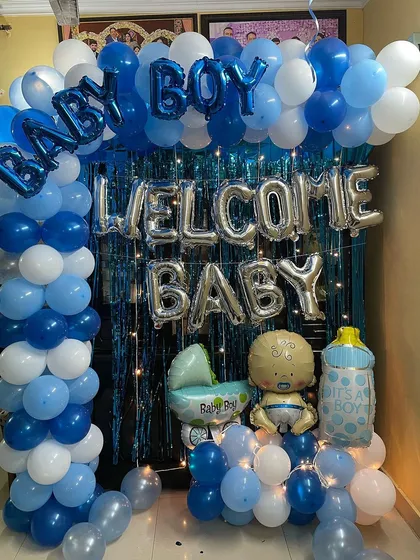 A classic "Welcome Baby Boy" decoration for a home. This setup includes a blue and white balloon arch over a shimmering blue foil curtain, with "WELCOME BABY" and "BABY BOY" foil letters and cute baby-themed props.