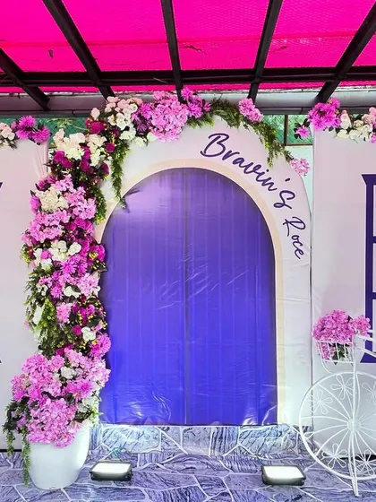 A vibrant and picturesque setup for a Roce ceremony. We created a backdrop resembling a European storefront with a purple door and windows, adorned with beautiful purple and white flowers.