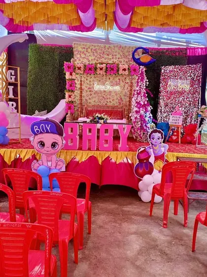 A complete baby shower stage inside a pandal, with seating for guests and cute baby-themed character cutouts.