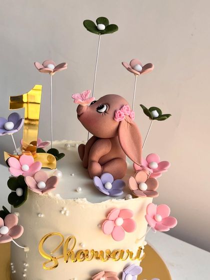 A close-up of the dreamy first birthday cake featuring a hand-sculpted pink elephant surrounded by delicate, multi-colored flowers.