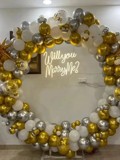 For that unforgettable moment, I design stunning proposal backdrops. This setup features a large ring decorated with gold, silver, and white balloons, with a "Will you Marry Me?" neon sign to make the question pop.