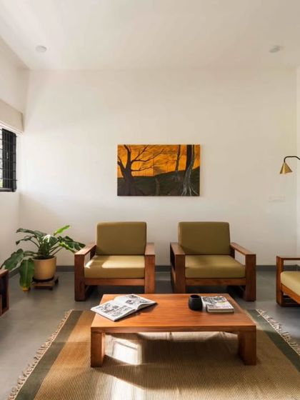 The living room is arranged with simple, modern wooden furniture. Large windows ensure the space is filled with natural light, while indoor plants help to blur the boundary between inside and out.