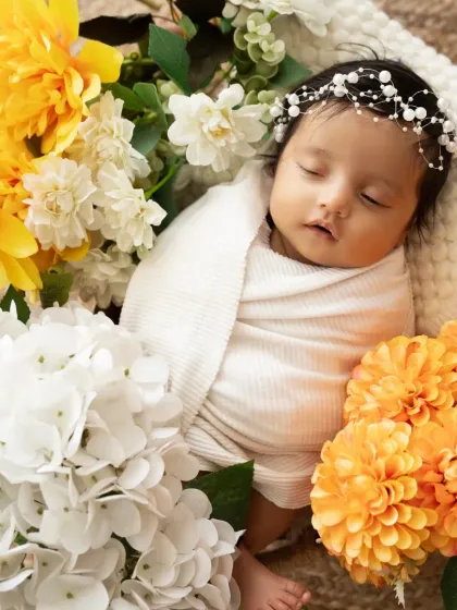 A peaceful newborn wearing a delicate pearl headband, nestled among a beautiful arrangement of fresh flowers. We have a wide selection of accessories for your session.