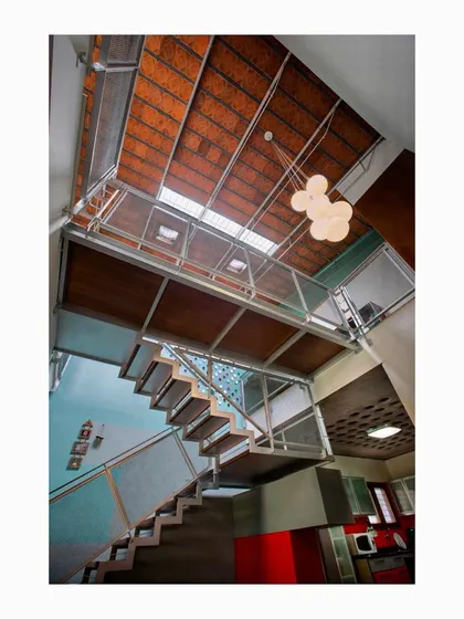 The Interlocking House features a fabricated light internal staircase with a woven steel mesh railing. This transparent structure allows light from the skylights above to filter down to the lower level, while beer bottle ends embedded in the wall create playful patterns of light.