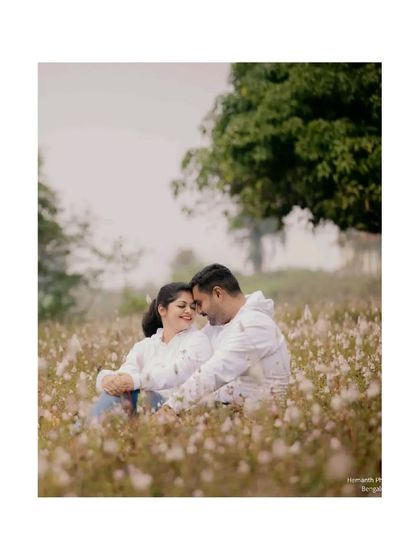 A couple sits together in a field of fluffy white cotton plants, sharing an intimate moment. The soft texture of the field creates a dreamy, romantic setting.
