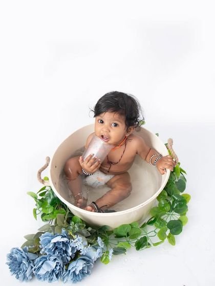 A simple and classic bathtub session against a clean white background. The focus is all on the baby's curious expression as he plays in the water, surrounded by a garland of blue flowers.
