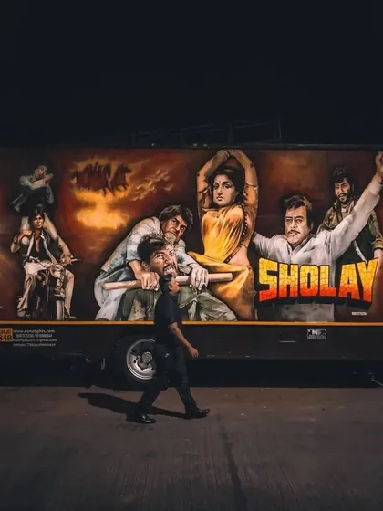 A classic, hand-painted mural of the iconic "Sholay" movie poster on the side of a truck. This is mobile street art, carrying a piece of Bollywood history through the lanes of Mumbai.