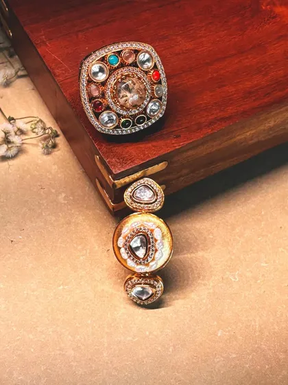 A close-up of two statement rings, one with a large navratna setting and the other with a more minimalist polki design.