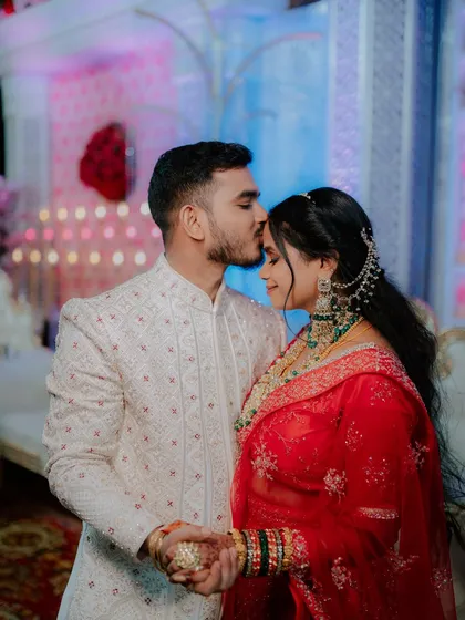 A tender moment between the bride and groom during their wedding reception, with the groom placing a gentle kiss on her forehead.