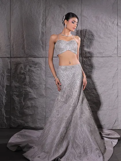 A full-length view of this unconventional bridal gown. The sleek silhouette and intricate silver embroidery are complemented by a clean, sophisticated makeup look.
