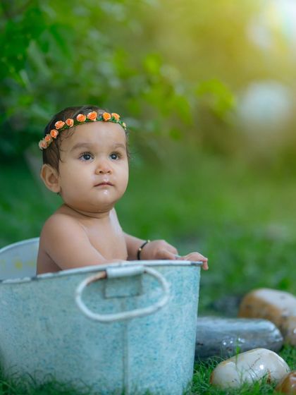 An outdoor bath time-themed portrait. The natural light and green surroundings add a fresh, sweet feel to this baby's photoshoot in a rustic metal tub.