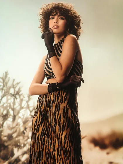 A desert landscape projection provides a warm, desolate backdrop. The lighting is designed to feel like the hot sun, creating a high-contrast, high-fashion image.