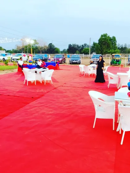 We cover large outdoor areas with carpeting to create a clean and defined party space. Here, a red carpet covers the lawn, with white garden chairs and tables set up for guests.