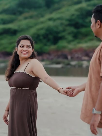 The groom-to-be leads his partner by the hand, both sharing a smile. This candid shot captures a moment of gentle guidance and shared happiness on the beach.