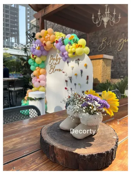 A creative centerpiece using baby shoes as a vase for fresh flowers, placed on a rustic wood slice. It's these small, thoughtful details that make a celebration special.