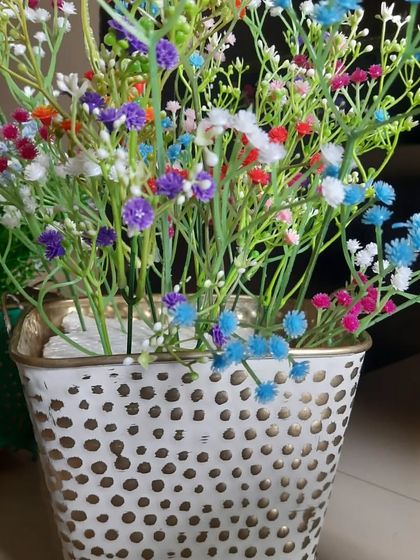A distressed white metal bucket planter filled with a vibrant mix of colourful artificial flowers. This piece has a lovely farmhouse-chic vibe.