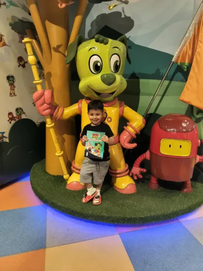 A young superstar poses proudly with his coloring book next to the statues of Tinga Dojo and Popsy.