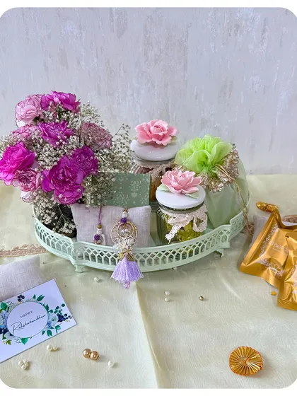 This beautiful mint green tray hamper is decorated with fresh flowers and includes jars of our gourmet nuts and a Rakhi set.