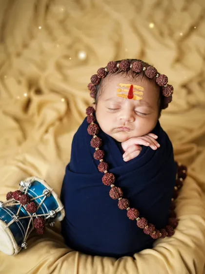 A full-length view of the newborn Shiva setup. The combination of the blue wrap, rudraksha beads, and damru creates a powerful image.