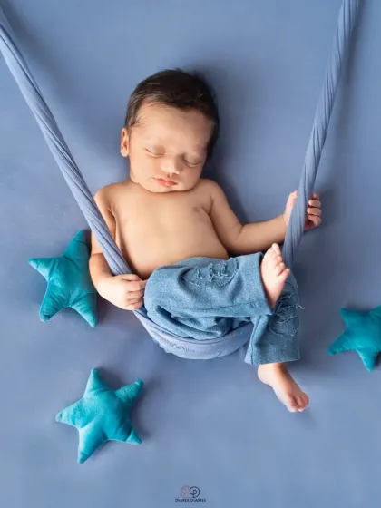 A newborn boy sleeps peacefully in a blue sling hammock, surrounded by plush blue stars. This simple setup creates a dreamy, celestial-themed newborn portrait.