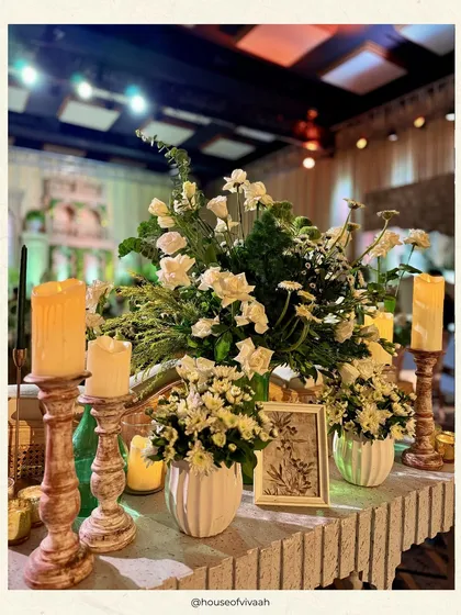 A console table styled with an abundance of white florals, rustic wooden candle holders, and framed botanical prints, showcasing a chic and layered decor approach.