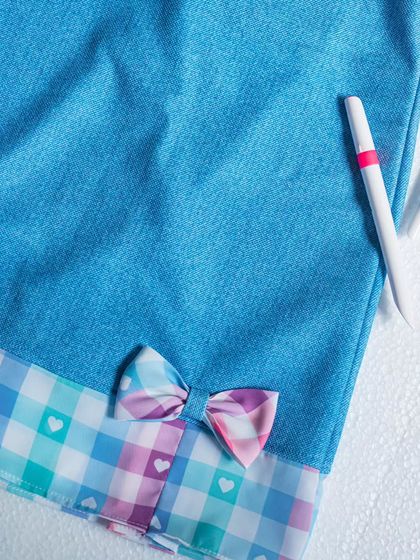 A detailed shot of this denim and plaid dress. The heart-print plaid fabric is pleated at the hem, and a small bow ties the colors together perfectly.