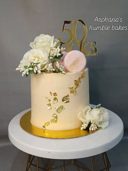 A classy and simple cake for a 50th birthday, decorated with white roses, macarons, and gold leaf.
