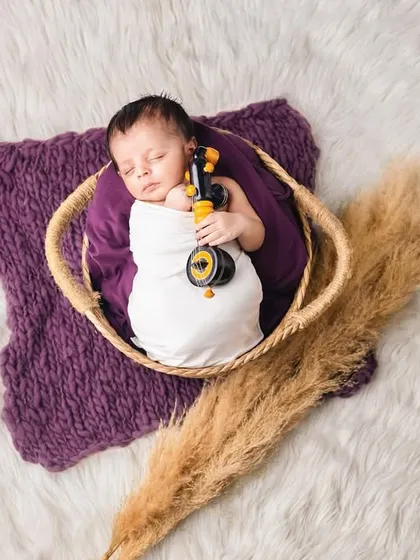 A newborn sleeping in a small basket, holding a miniature sitar, combining music and tranquility.