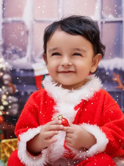 A close-up of a smiling baby Santa, holding a tiny ornament. His happy expression is contagious.