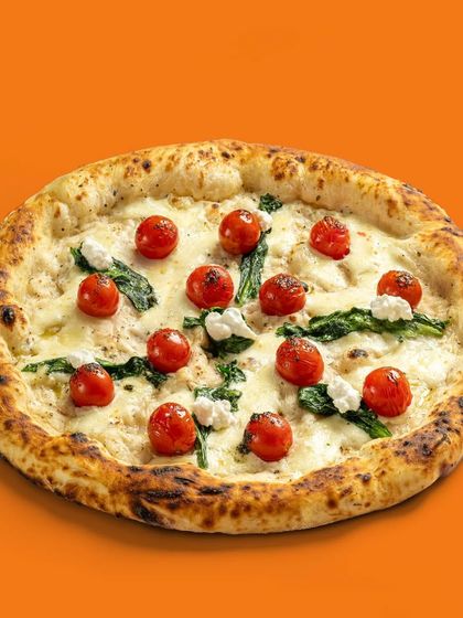 A white sauce pizza with cherry tomatoes and spinach, a lighter and fresher pizza option.