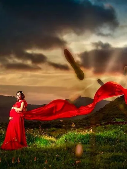 This dramatic red trail gown isn't just for pre-weddings; it's also a stunning choice for a powerful and beautiful maternity shoot. The flowing fabric creates a breathtaking silhouette against a natural landscape.