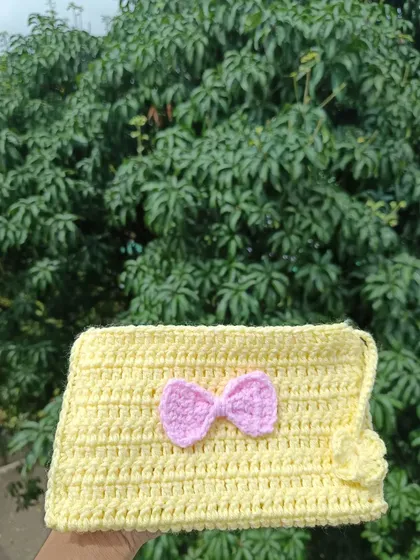 A handmade crochet pouch in yellow with a pink bow accent. These are perfect for holding small essentials like coins, keys, or makeup.