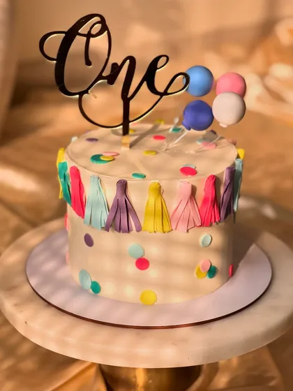 A festive and colorful cake for a first birthday party. This lemon-flavored cake is decorated with a fun tassel garland, confetti dots, and a balloon topper.