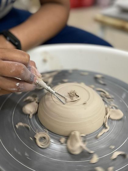 A close-up of the trimming process, where small ribbons of clay are carved away to perfect the shape of a wheel-thrown bowl.