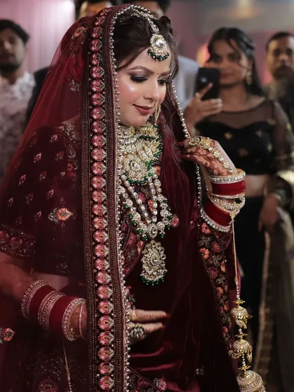 A candid shot of the bride during her entrance. The soft lighting highlights her glowing skin and the intricate details of her maroon velvet lehenga.